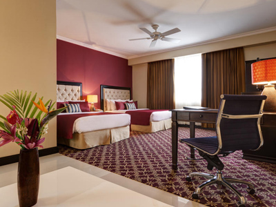 Picture of an upgraded room at the Costa Rica Medical Center Inn, San Jose, Costa Rica.  The picture shows two beds and a vase of flowers in the foreground.