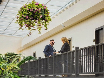 Picture of an interior corridor at the Costa Rica Medical Center Inn, San Jose, Costa Rica.  The picture shows a happy couple on the second floor framed by an overhead hanging plant.